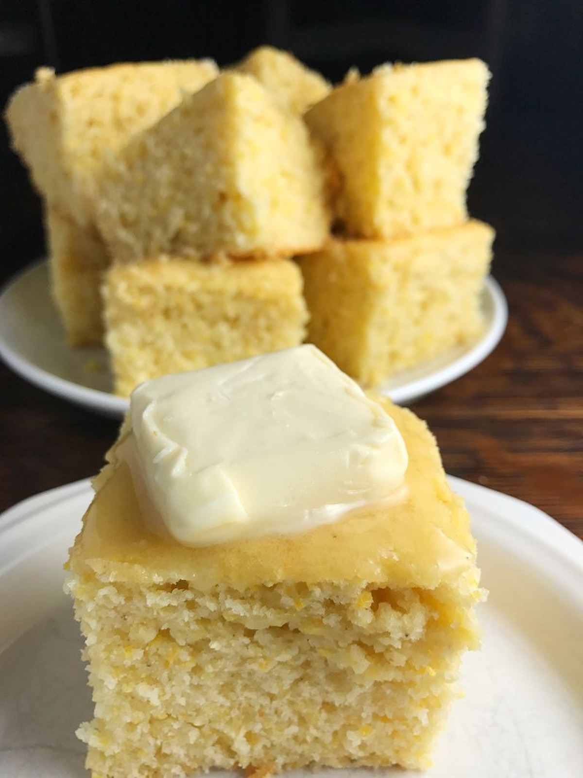Sweet Dairy-Free Cornbread cut into pieces at stacked on a plate in the background with a single piece on a small white plate in front of it.