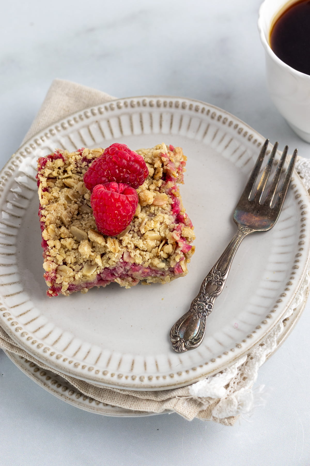 gluten free raspberry bars plated with fork, napkin and a cup of coffee
