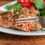 marinated salmon on white plate with fork cutting it